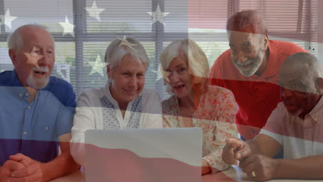 animation of flag of usa over diverse senior people using laptop