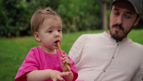 a father and his baby daughter are enjoying a picnic in the park.