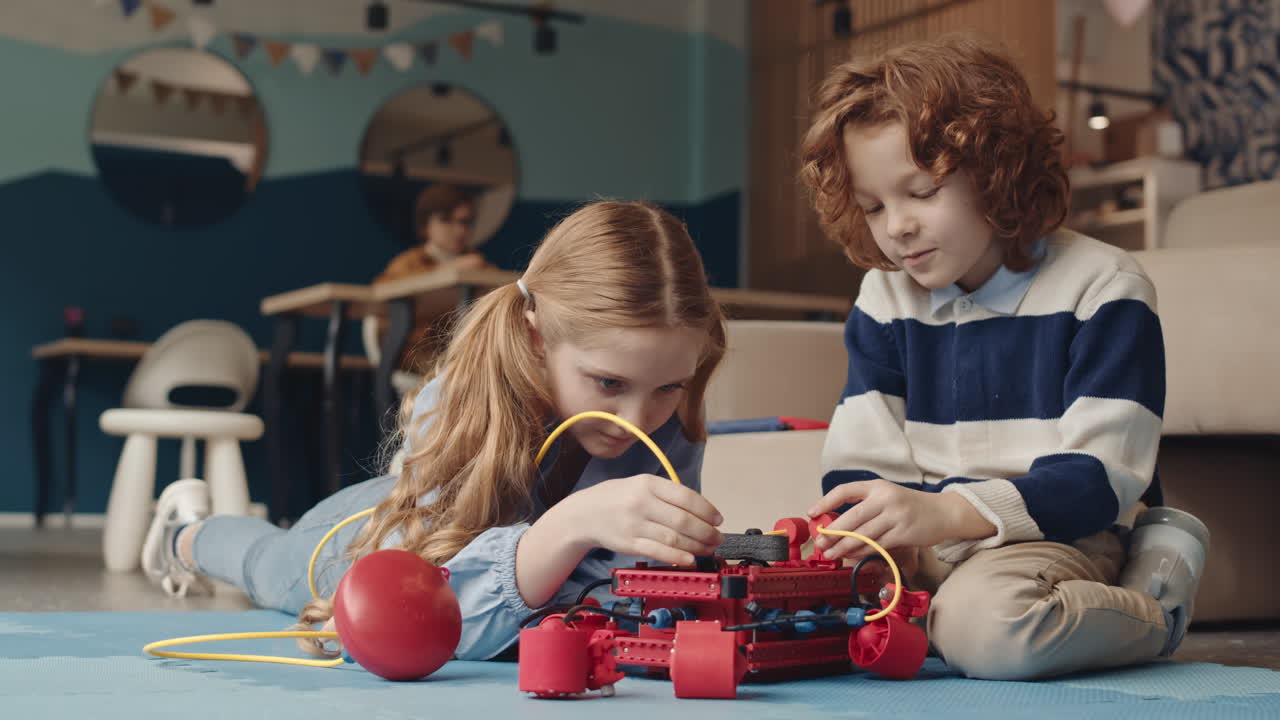 Two children building a robot on the floor in a classroom