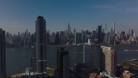 Forwards-fly-around-high-rise-apartment-buildings.-Revealing-panoramic-view-of-river-and-tall-downtown-skyscrapers.-Manhattan,-New-York-City,-USA