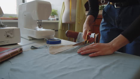 female dressmaker using scissors while cutting fabric at work