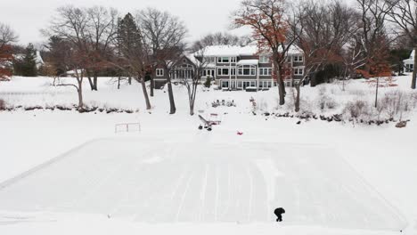 aerial, person clearing snow to make a small hockey ice rink on a frozen lake outside of house