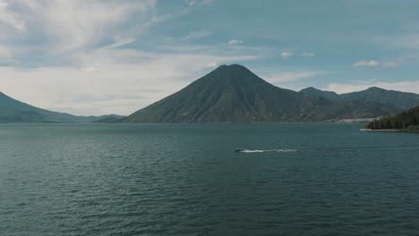 drone aerial view of a boat traveling on lake atitlan, guatemala with beautiful volcano and blue water landscape