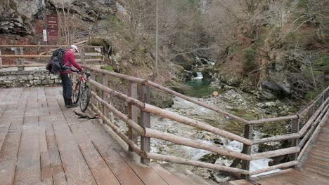 Walking-a-bike-up-to-a-fence-to-lock-up-the-bike-with-the-river-stream-running-next-to-it-and-a-wooden-viewpoint