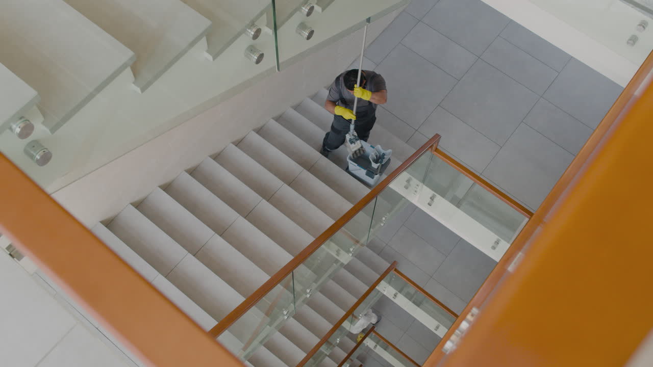 vista superior del hombre de limpieza árabe con guantes limpiando escaleras con fregona dentro de un edificio de oficinas 2