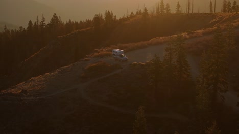 rv parked on a mountain trail at sunset surrounded by pine trees and golden light