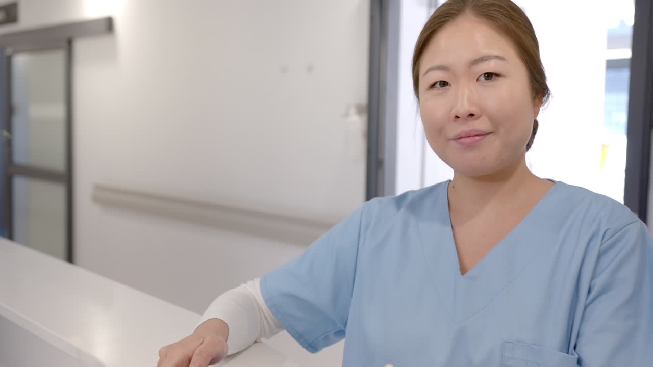 병원 접수 데스크에서 태블릿을 사용하는 행복한 아시아 여성 의사의 슬로우 모션 초상화