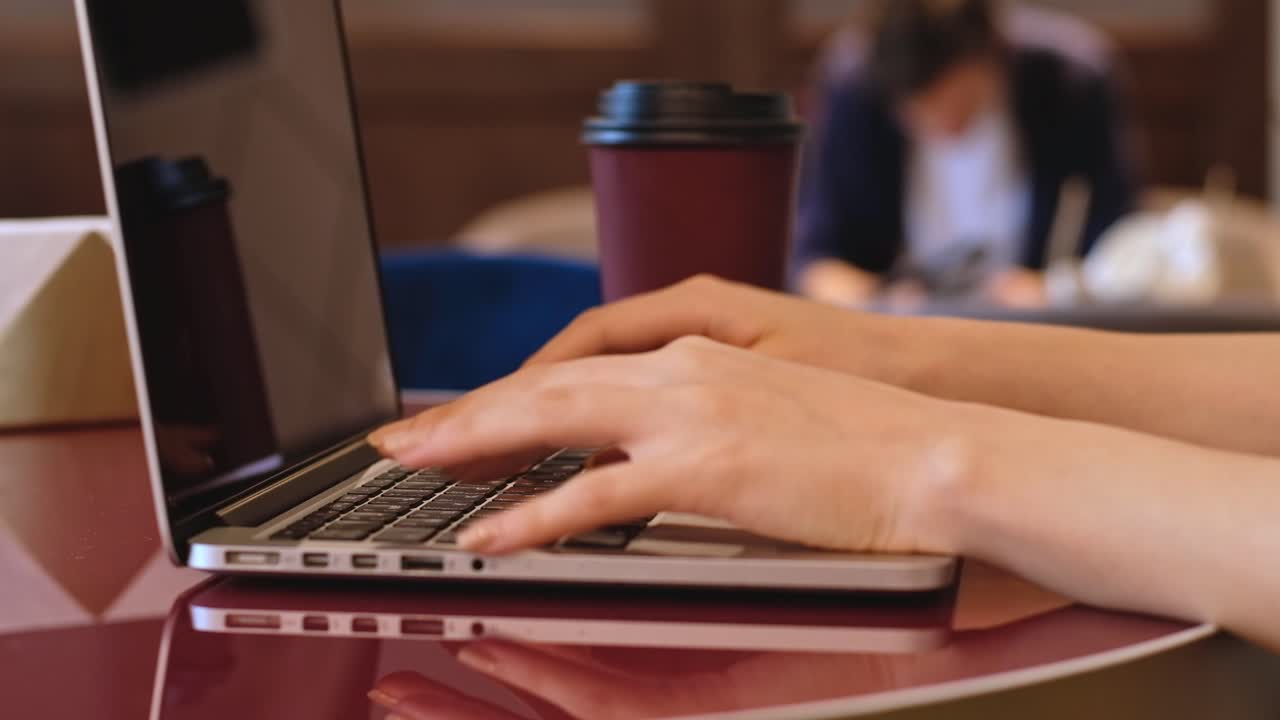 Young girl typing on laptop and drink coffee in a cafe