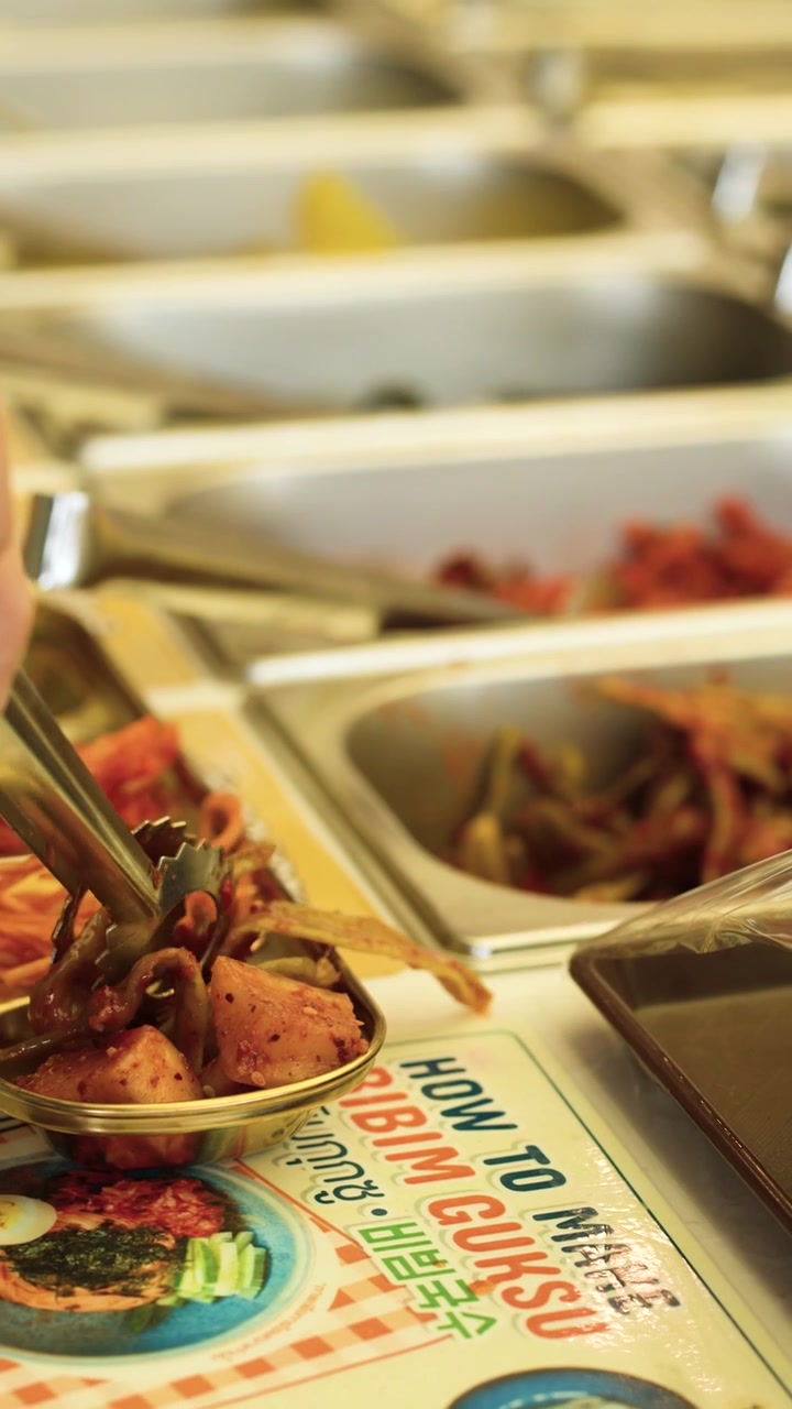 Primo piano di una persona che seleziona vari banchan da vassoi di metallo a un buffet di ristorante