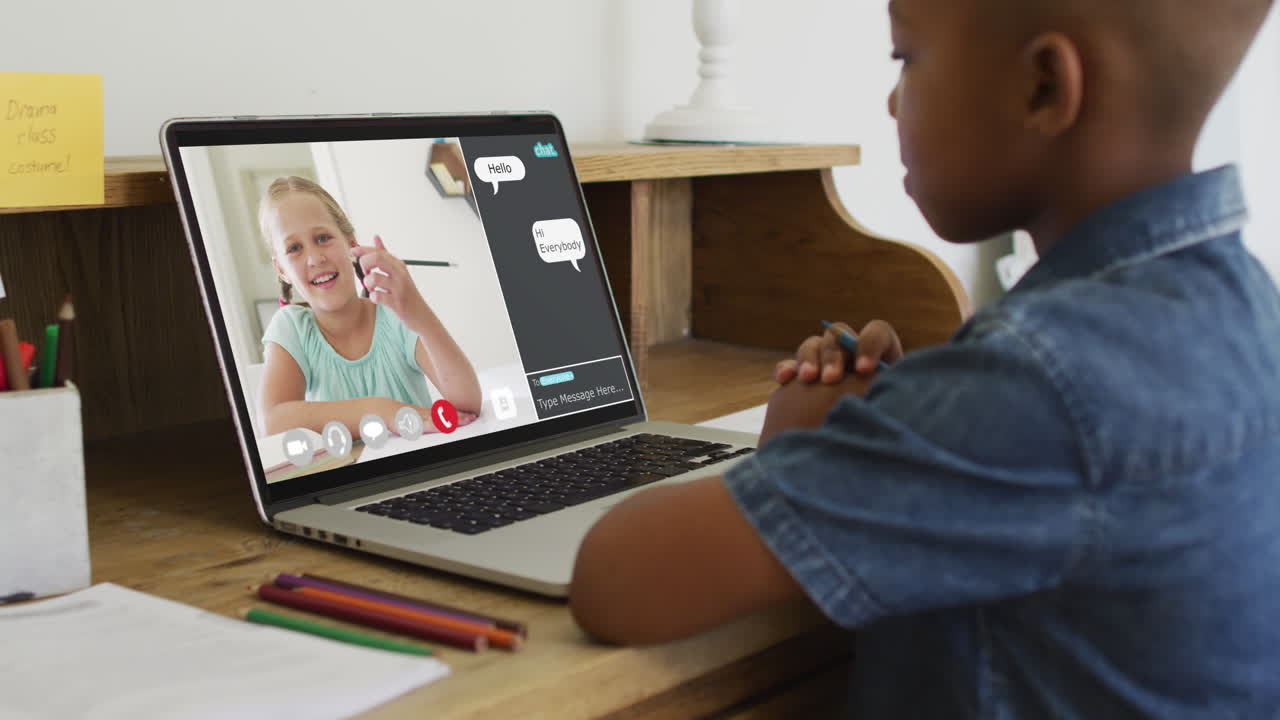 Schoolboy using laptop for online lesson at home, with schoolgirl and web chat on screen