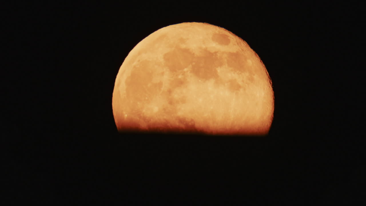 Large full moon rising against a dark night sky with clear details and dramatic atmosphere