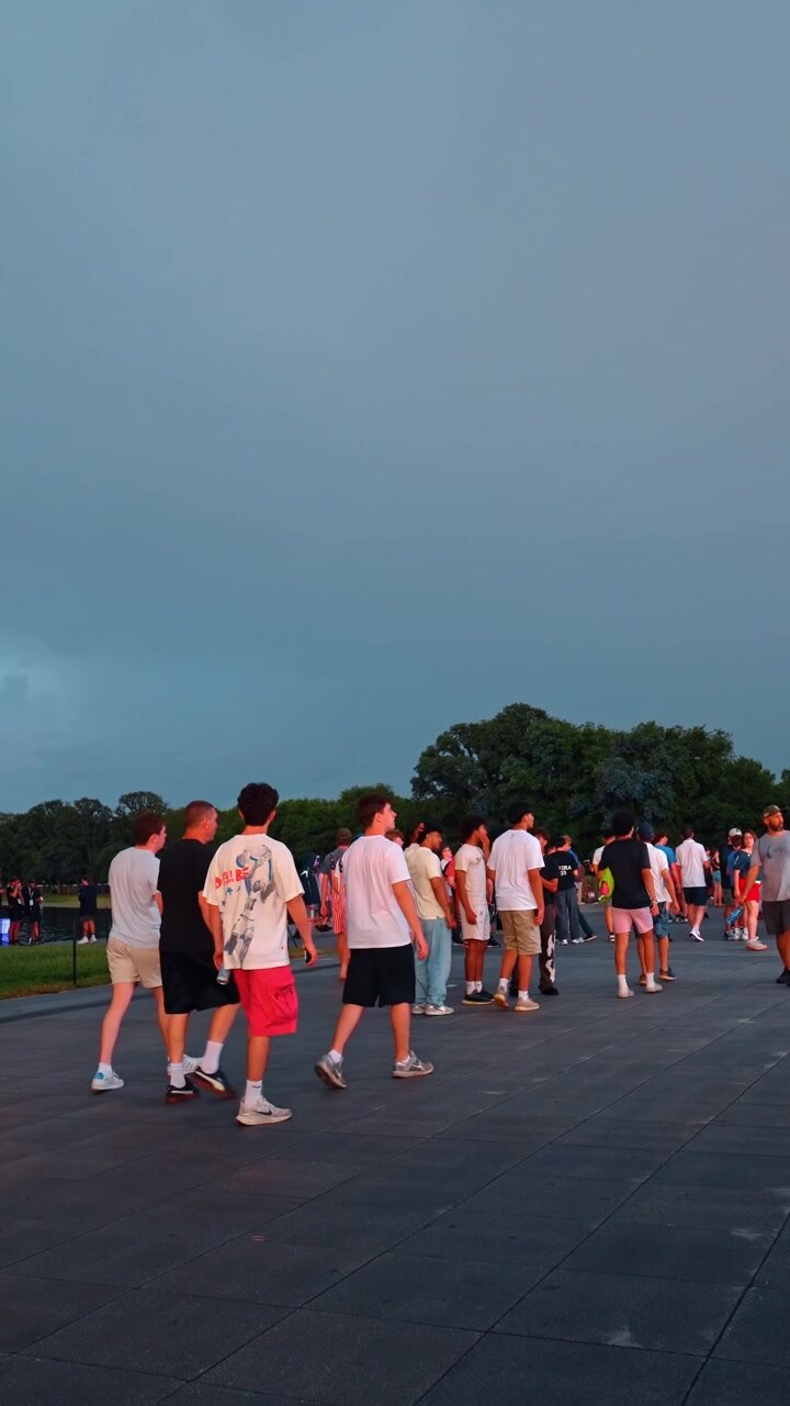 Washington, USA, 1 giugno 2026: folla di persone che cammina all'aperto su una piazza pavimentata. Giovani che indossano abiti con la bandiera americana camminano sotto un cielo scuro e coperto a Washington DC