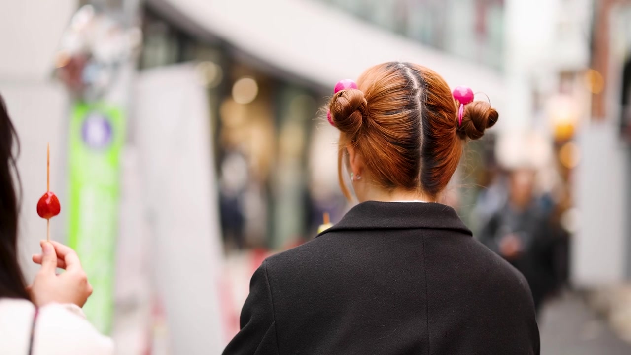 Vista posteriore di una donna con chignon spaziali che mangia frutta candita per strada ad Harajuku, Tokyo.