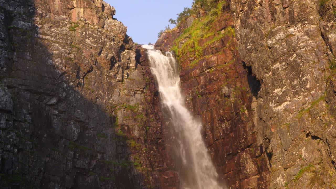 tiro inclinado de gran angular de la cascada njupeskär, sumergiendo agua dulce entre el cañón erosionado, iluminado por el sol dorado de la mañana de verano en el parque nacional fulufjället, en särna, suecia
