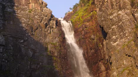 Wide-angle-tilt-up-shot-of-Njupeskär-waterfall,-plunging-fresh-water-between-eroded-canyon,-lit-by-midsummer-morning-golden-sun-at-Fulufjället-National-Park,-in-Särna,-Sweden