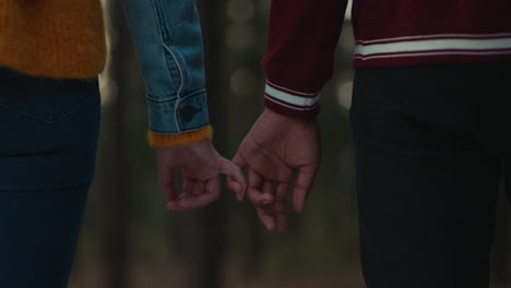 teenage couple holding hands in forest at sunset boyfriend playfully holds girlfriends pinky finger sharing romantic connection in woods happy young lovers