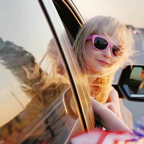 una niña pequeña con gafas rosas mira por la ventana del auto