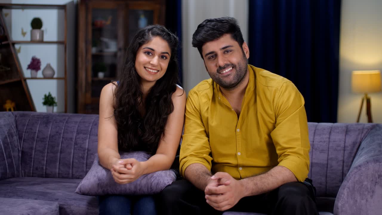 A smiling Indian couple posing together for the camera in their living room - a modern lifestyle, photogenic