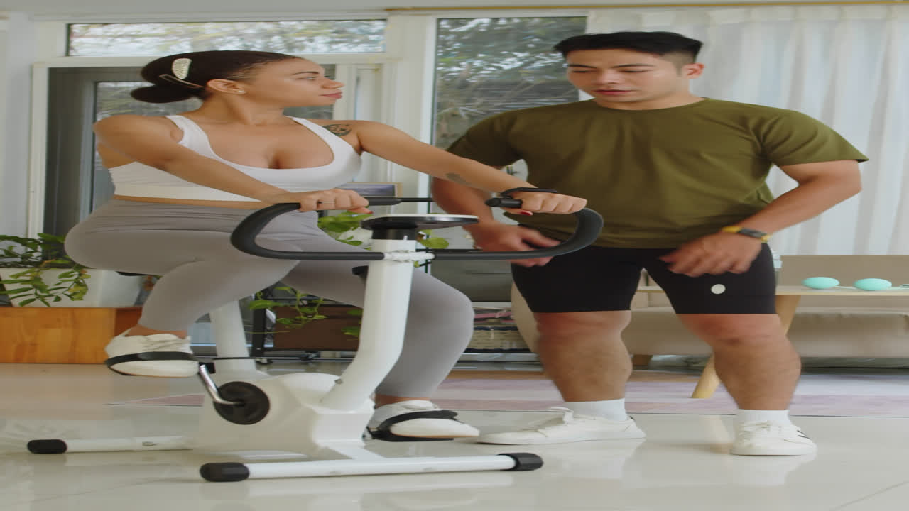 Trainer Helping Woman with Exercise on Fitness Bike Indoors
