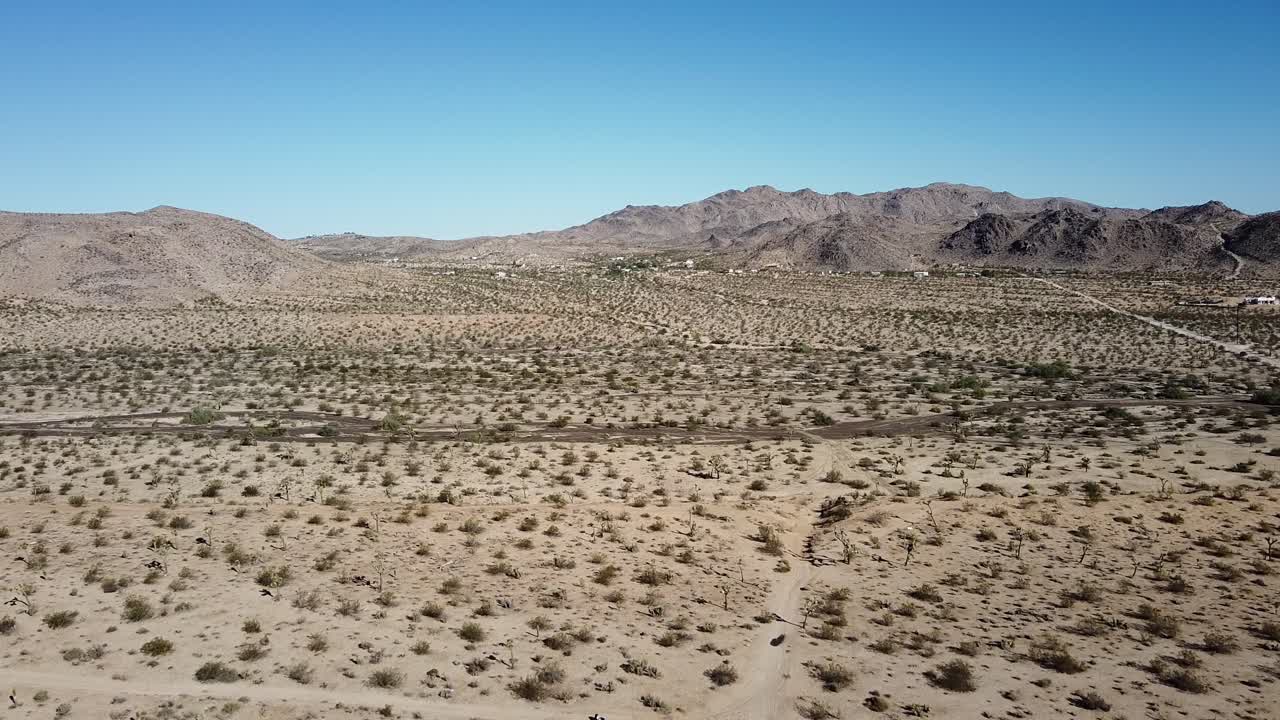 toma aérea cinematográfica del desierto con vegetación baja, montañas en el fondo y cielo azul