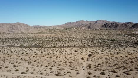 toma aérea cinematográfica del desierto con vegetación baja, montañas en el fondo y cielo azul