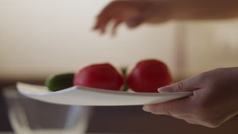 lady puts juicy cucumber to tomatoes on white square plate