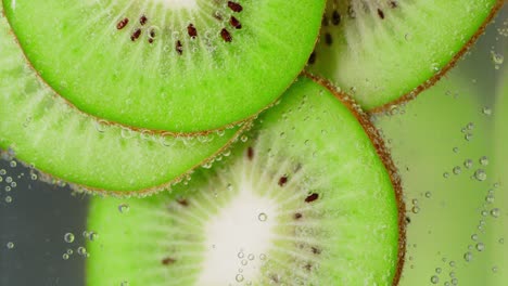 round slices of fresh kiwi under water with air bubbles.