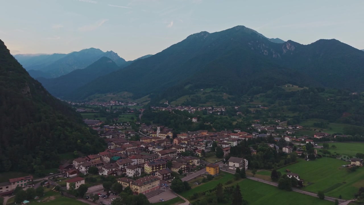 Veduta aerea con drone del villaggio alpino di Bezzecca con tetti in terracotta e campanile della chiesa, immerso in una verde valle di montagna.