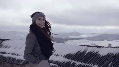 girl in the grey coat and black scarf standing in the cold winter wind and enjoying snowy scenery in the distance, 50p