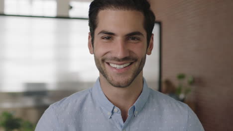 Retrato-De-Cerca-De-Un-Joven-Empresario-Exitoso-Del-Medio-Oriente-Mirando-La-Cámara-Sonriendo-Feliz-En-El-Fondo-Del-Espacio-De-Trabajo-De-Oficina