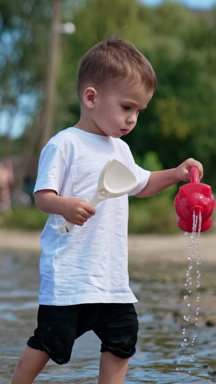 Small kid having fun at river sand beach. Boy playing on the beach with water. Vertical video