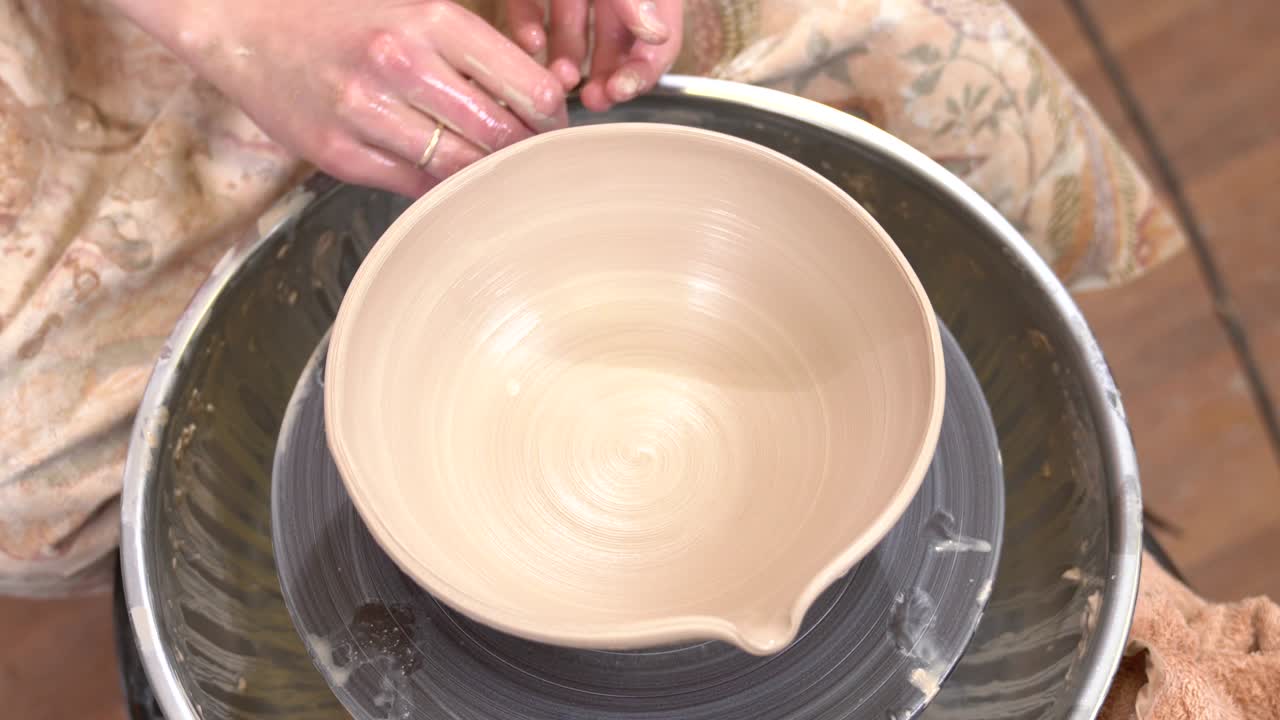 Closeup top view of potter fine-tuning a clayware shape with wet fingers in ceramic workshop.