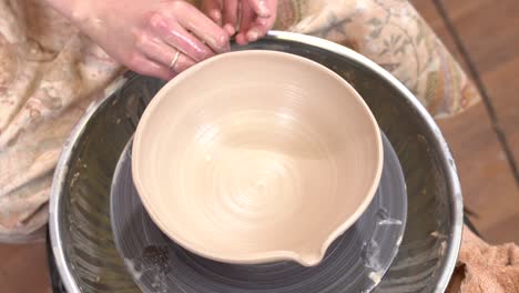 closeup top view of potter fine-tuning a clayware shape with wet fingers in ceramic workshop.