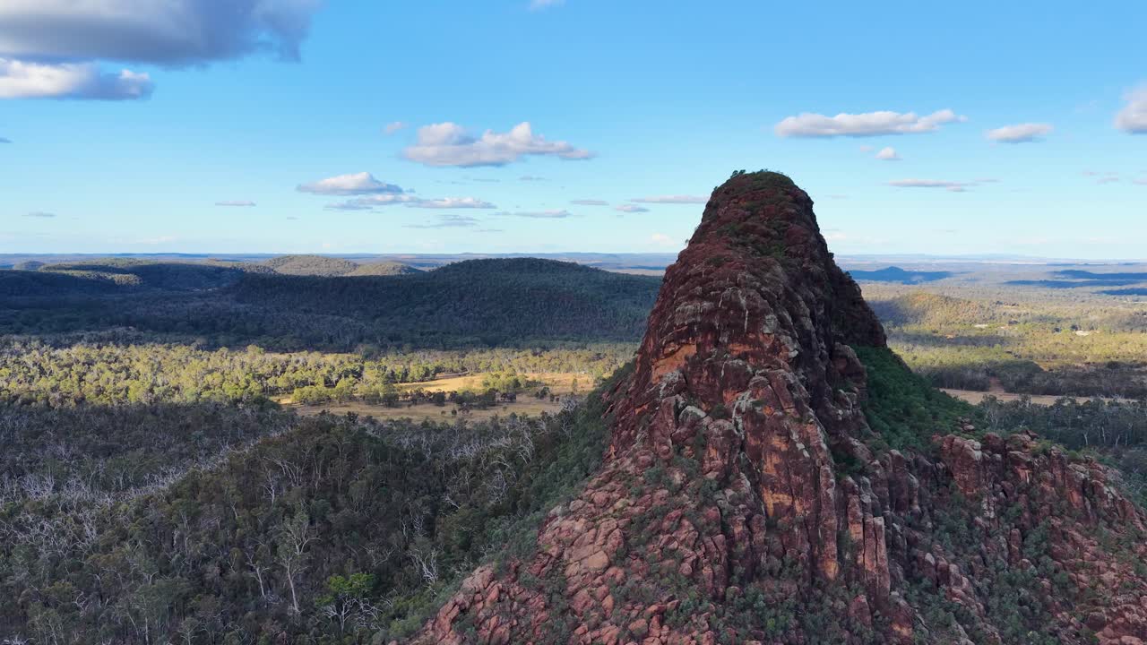 Drone glides over volcanic outcrop, Timor Rock, revealing vast Australian bushland under daylight
