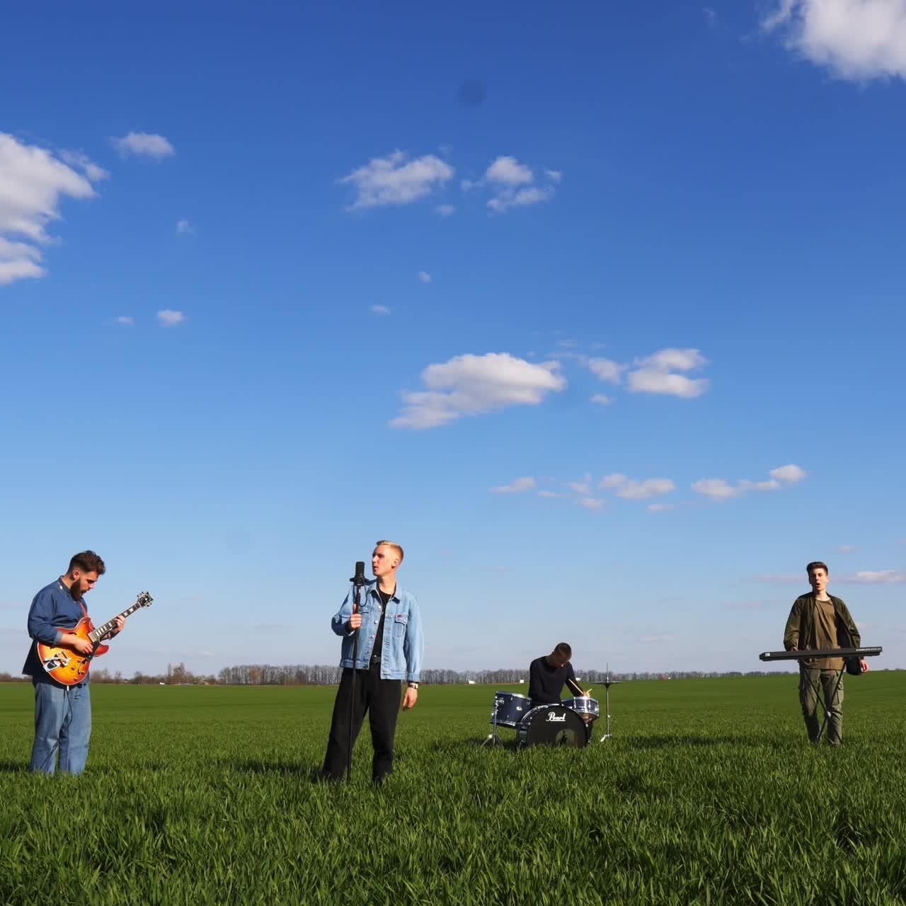 Male music band playing and singing outside the city. Boys' band performing in the green field on sunny day