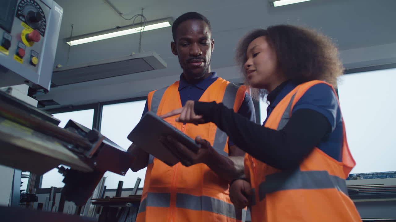 Due operai in un impianto industriale guardano un tablet discutendo di produzione e digitale.