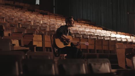 a handsome guy plays an acoustic guitar in an abandoned cinema. the musician sings a song and accompanies on the guitar