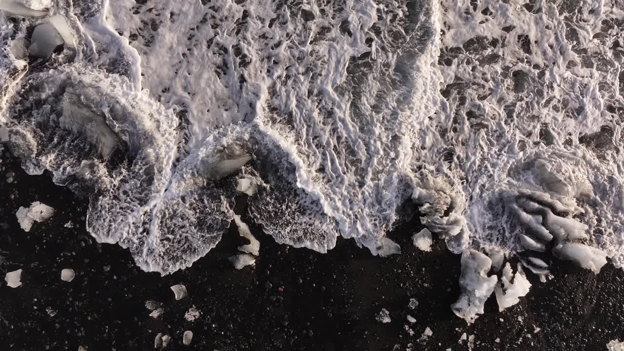 aerial top view ice blocks swirl in white surf on volcanic black beach Iceland