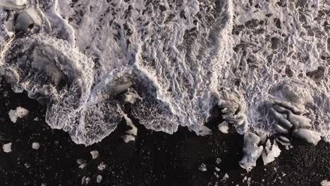 aerial top view ice blocks swirl in white surf on volcanic black beach iceland