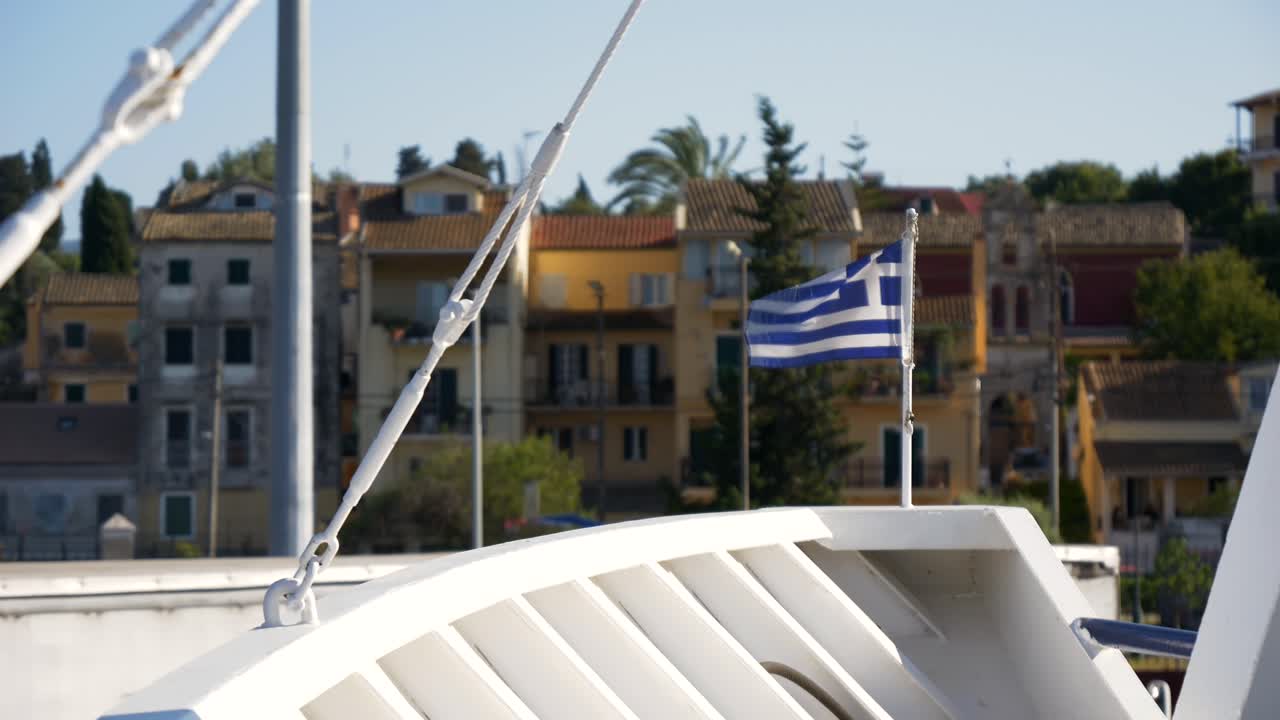 la bandera griega izada en la proa del barco, con edificios de la ciudad portuaria en el fondo en la isla de corfú
