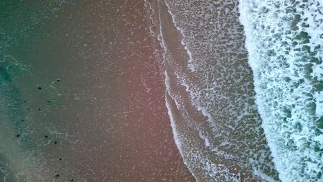 Aerial-begins-facing-down,-showing-the-sea-as-it-settles-on-a-beach-at-night