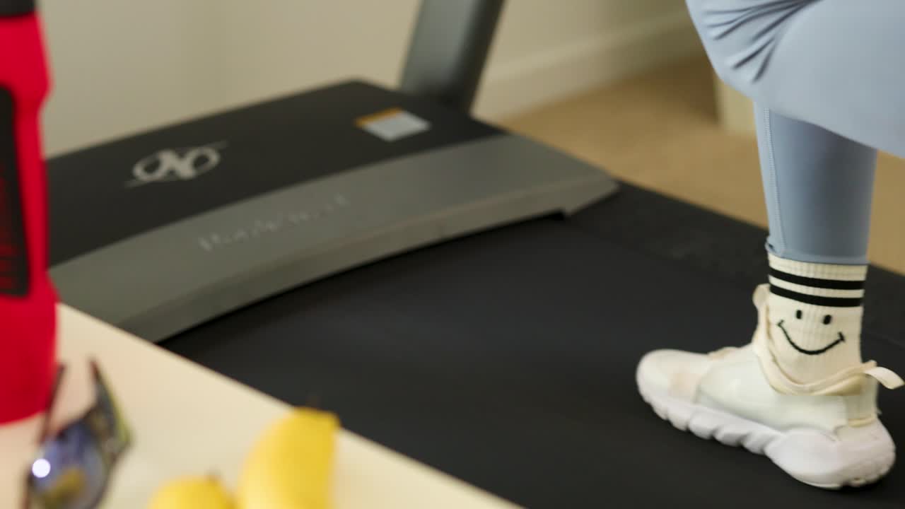 A person wearing athletic shoes and leggings walks on a treadmill in a well-lit gym environment