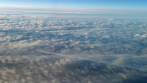 Vista-Increíble-Desde-La-Cabina-De-Un-Avión-Que-Vuela-Alto-Por-Encima-De-Las-Nubes-Dejando-Un-Largo-Rastro-De-Aire-De-Vapor-De-Condensación-Blanco-En-El-Cielo-Azul