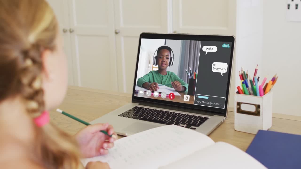 Schoolgirl using laptop for online lesson at home, with her school friend and web chat on screen