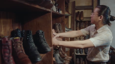 asian man putting old boots of shelves in antiques shop