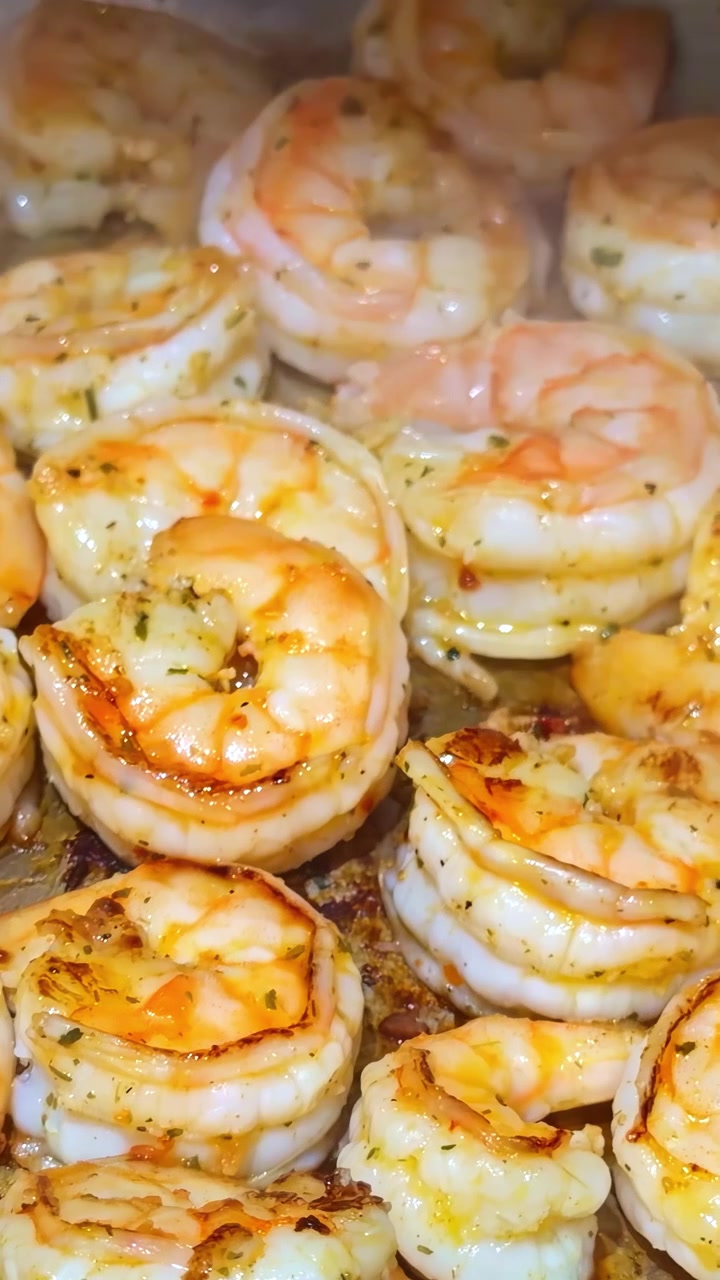 Vertical close-up of shrimp cooking in buttery sauce with herbs and steam, showing sizzling seafood preparation in a hot pan.