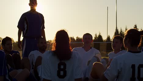 a soccer team sitting in a circle playing a fun game at sunset