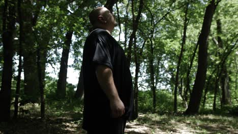 A-man-stands-in-the-forest-and-looks-up-at-trees-and-sunlight