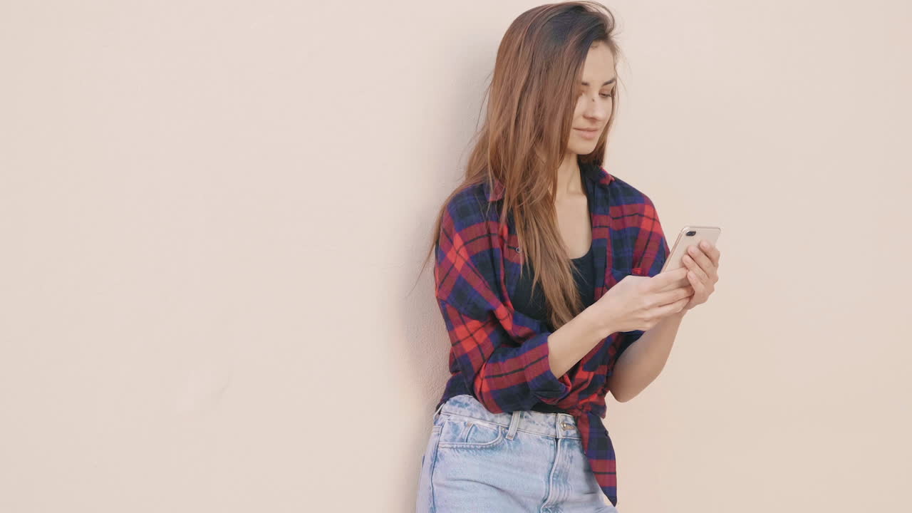 una joven apoyada contra una pared, enviando mensajes de texto en su teléfono.