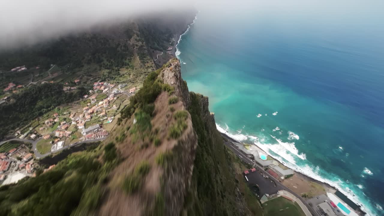 FPV drone moves above the forested cliffs of Lapas Negras in Madeira, revealing ocean views and a village below.
